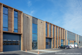 Modernes Gebäude von Blueprint Automation (PBA) im Holzstil mit mehreren großen Fenstern und Garagentoren. Im Vordergrund stehen Autos, während im Hintergrund ein blauer Himmel zu sehen ist.