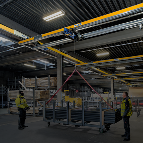 Zweiträgerkran ZHB hebt eine Last in einer Industriehalle, während Mitarbeiter den Vorgang begleiten.