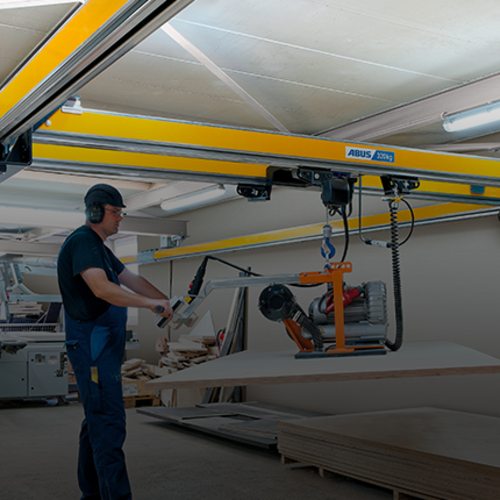 Mitarbeiter bedient einen Zweiträgerkran ZHB-X und hebt eine Last mit einem Kettenzug in einer Werkhalle.